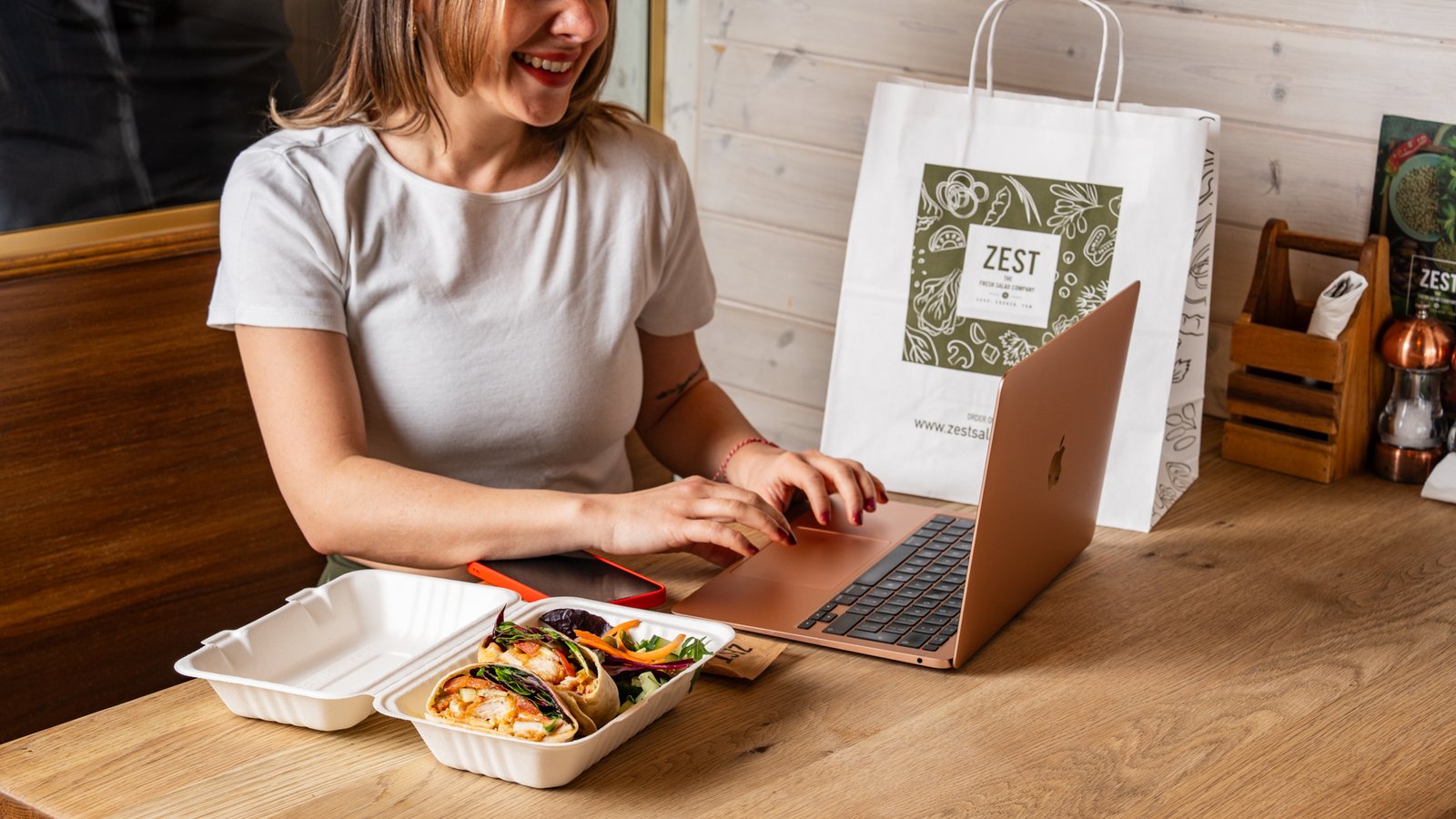 Customer working on laptop with fresh salad at Zest Salad Bar South Woodford